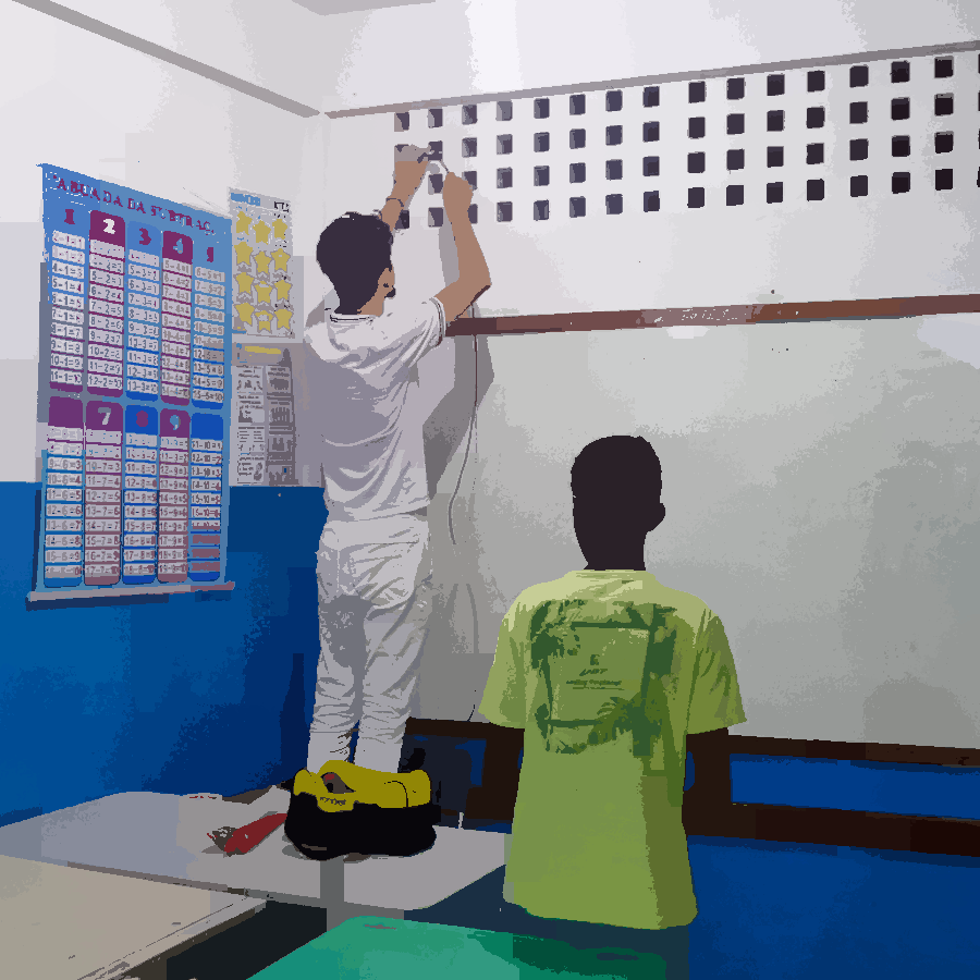 Nesta imagem podemos ver a instalação de um roteador em uma sala de aula. Podemos ver uma pessoas fazendo a instação da parede onde fica a louça, enquanto um estudante observa a ação.