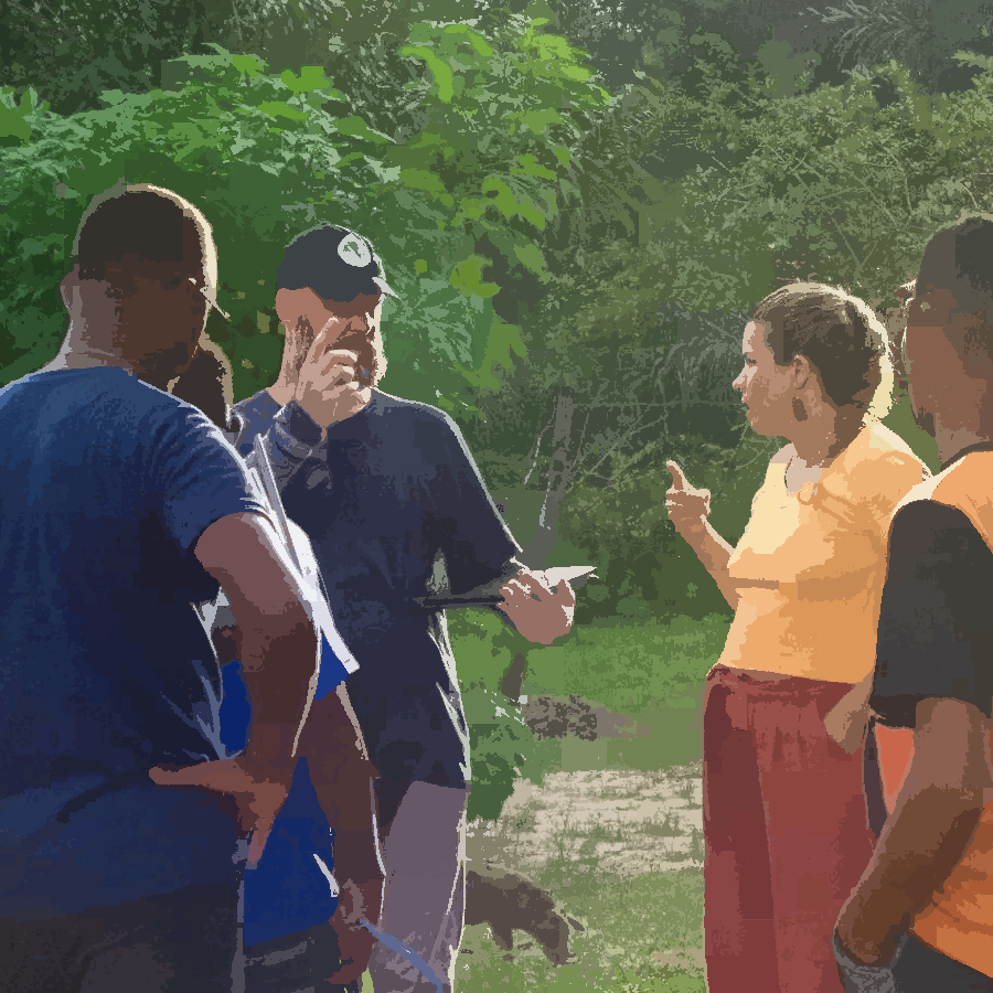 Na imagem podemos observar um grupo de pessoas em um círculo, conversando sobre o projeto, em um ambiente externo. Todas elas estão de pé.