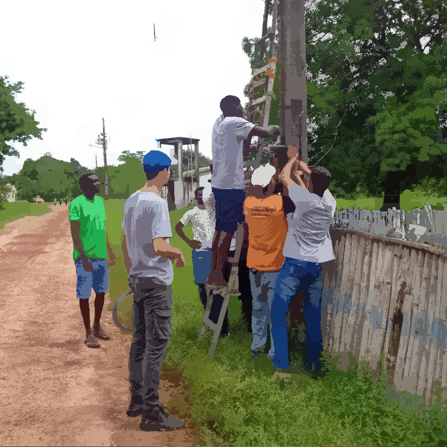 Na imagem podemos ver um grupo reunido ao redor de uma escada apoiada em um poste. Um jovem está na escada para colocar um roteador nesse poste. As outras pessoas estão auxiliando esse jovem e apoiando a escada.