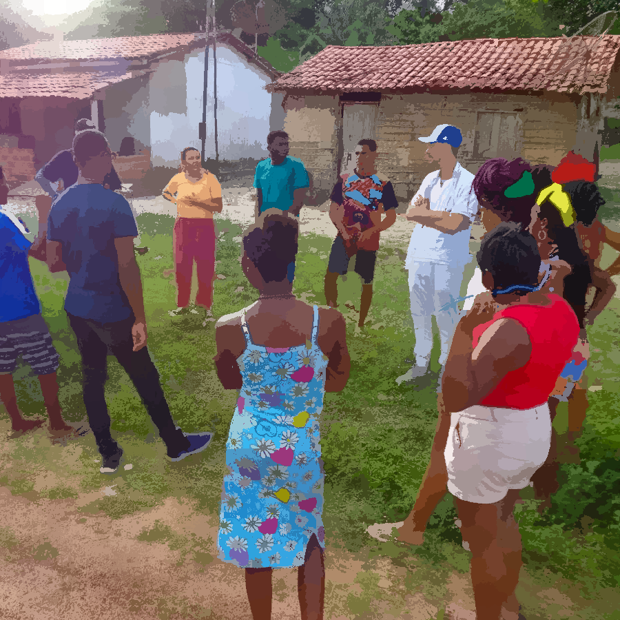 Na imagem, podemos ver um grupo de pessoas em pé, formando uma roda de conversa em um ambiente externo.